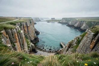 Paysage côtier romantique en Bretagne avec falaises de granit, baie turquoise et manoir en arrière-plan