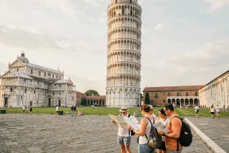 Vue grand angle de la tour de Pise avec des touristes consultant un guide de visite sur la Piazza dei Miracoli